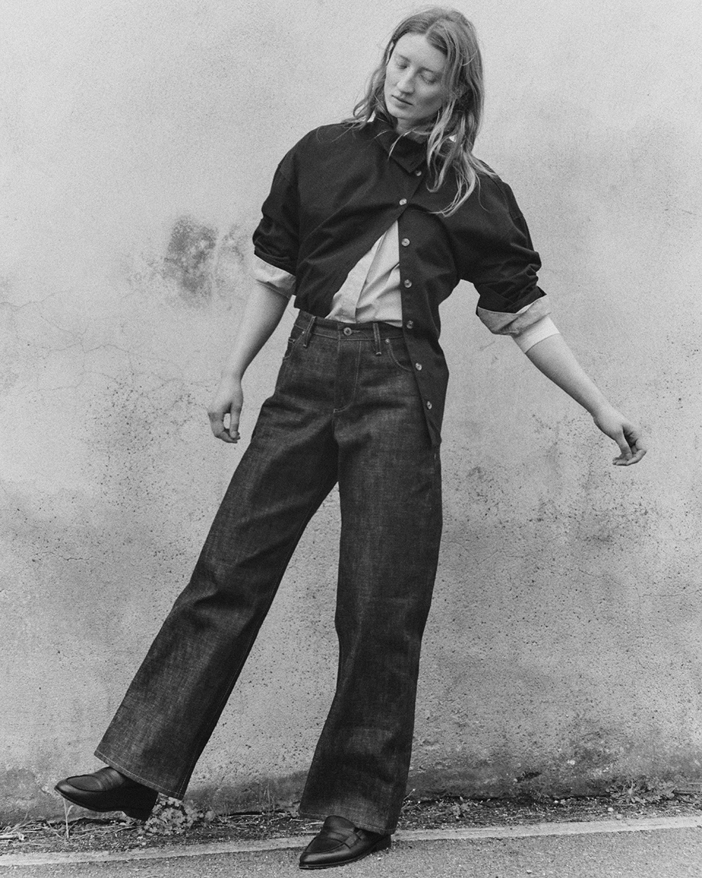 Black and white image of woman wearing Selvedge Edna jeans, a shirt and black boots. 
