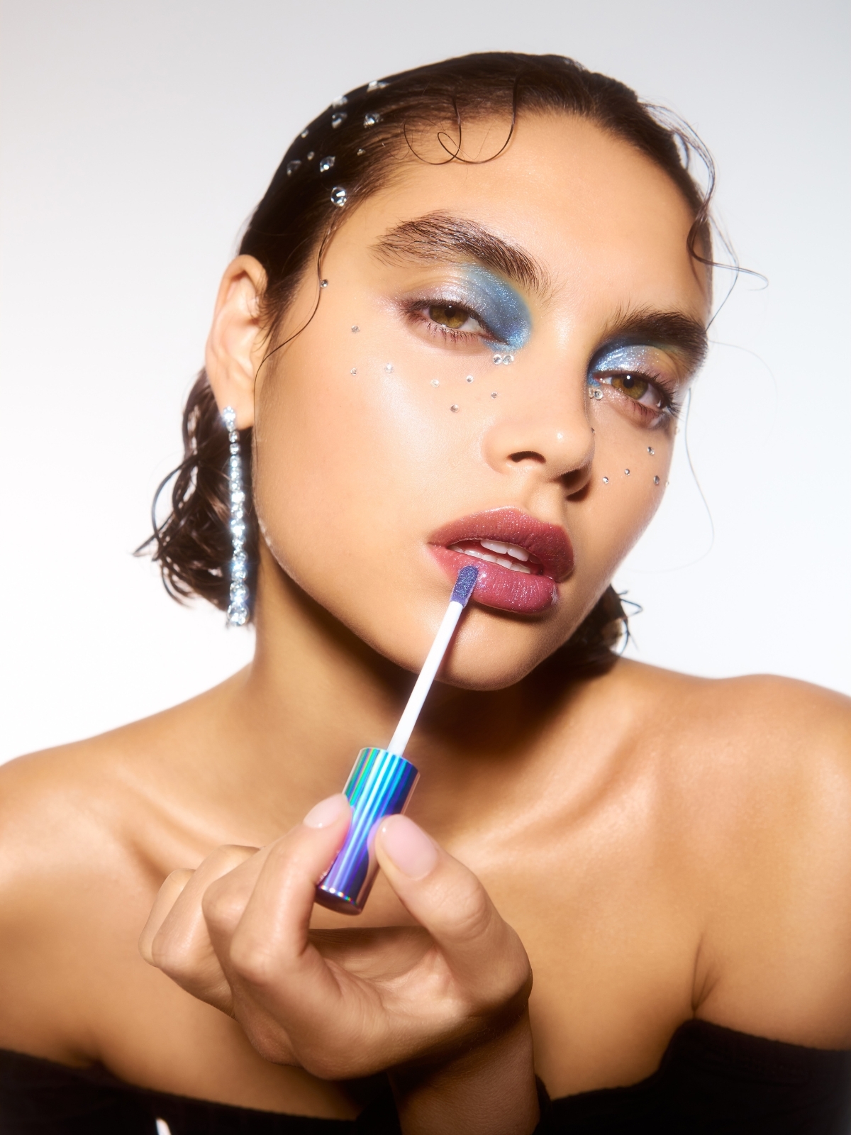 Model wearing blue eyeshadow and applying lip gloss