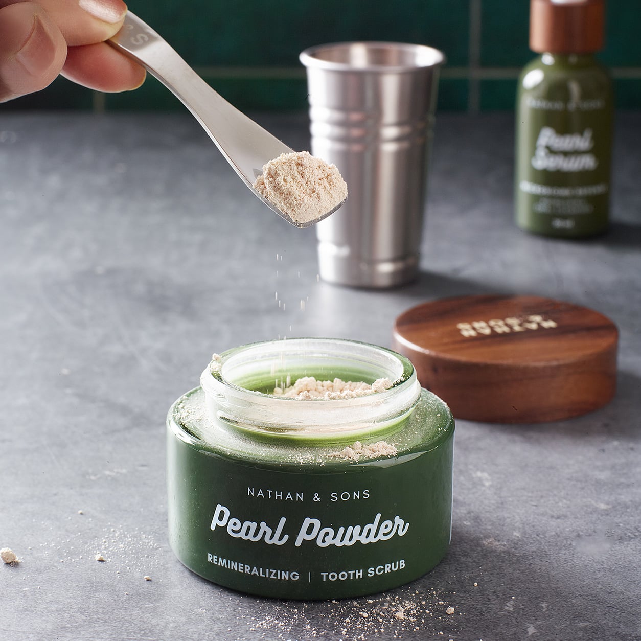 A close-up shot shows a hand holding a metal spoon with light-colored powder over an open green jar labeled 'NATHAN & SONS Pearl Powder REMINERALIZING...