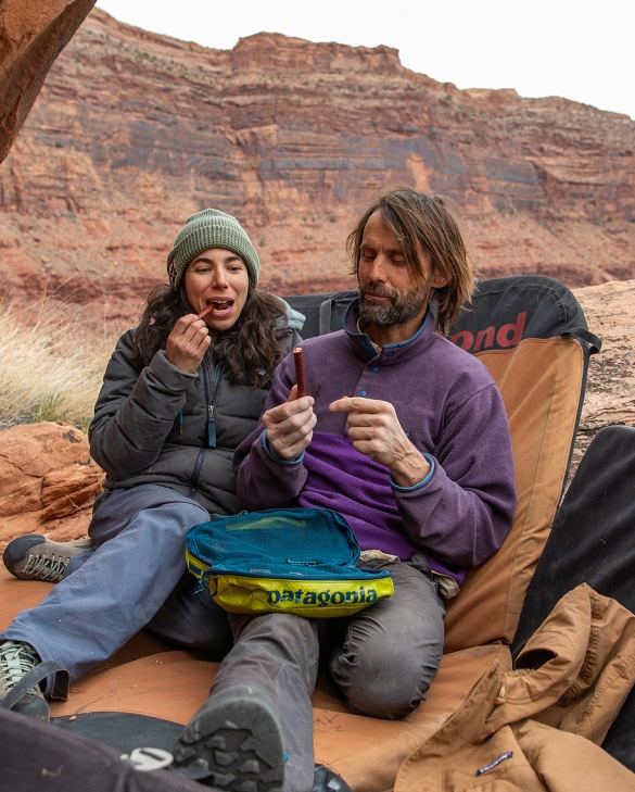 Meat Sticks. Two people eat meat sticks while sitting on climbing crash pads in red rock desert canyon country.