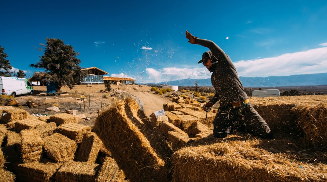 A person offloads straw bales from a truck trailer on a straw bale home construction site.