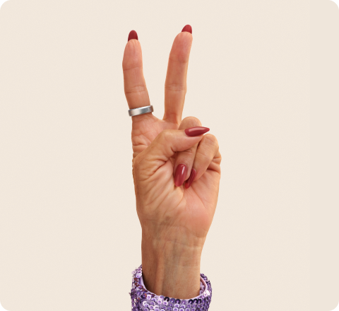 A hand making a peace sign, wearing a silver Oura Ring on the index finger.