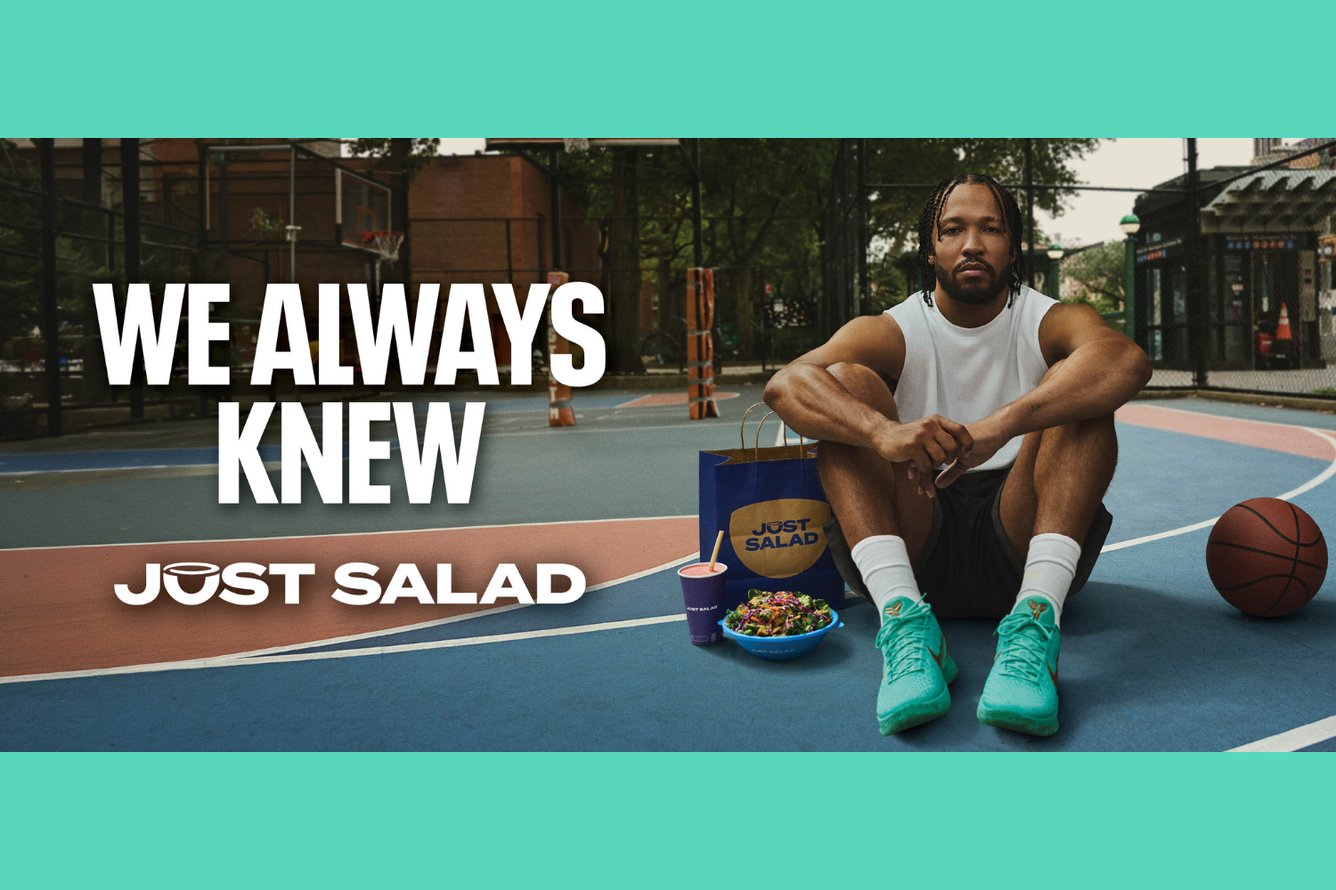 Jalen Brunson sits on an outdoor basketball court with a serious expression on his face, with a basketball to his left and a Just Salad meal to his right. The text WE ALWAYS KNEW: JUST SALAD