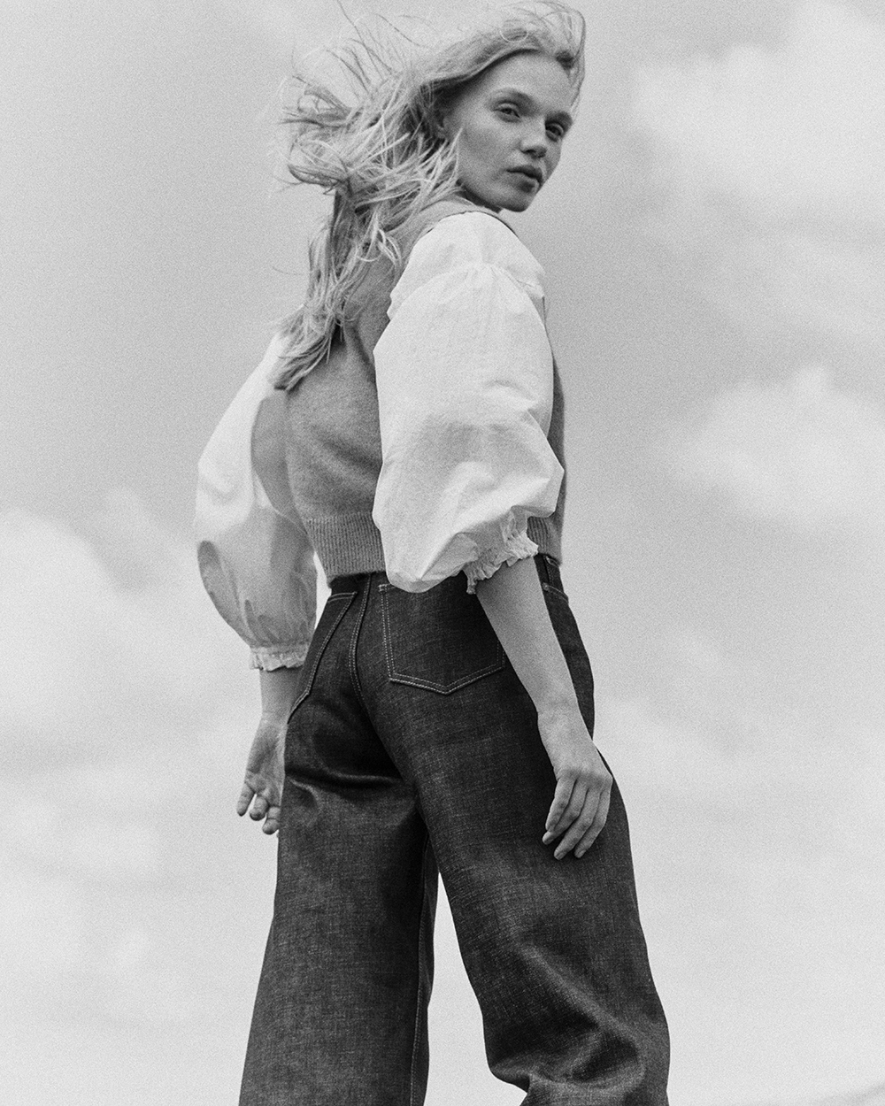 Black and white photo of woman wearing Edna selvedge jeans, a white shirt and sleeveless wool jumper.