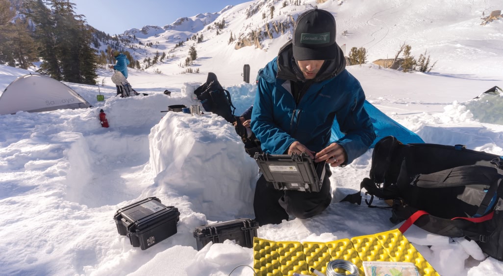 A person fiddles with audio recording equipment while camping in the snow.