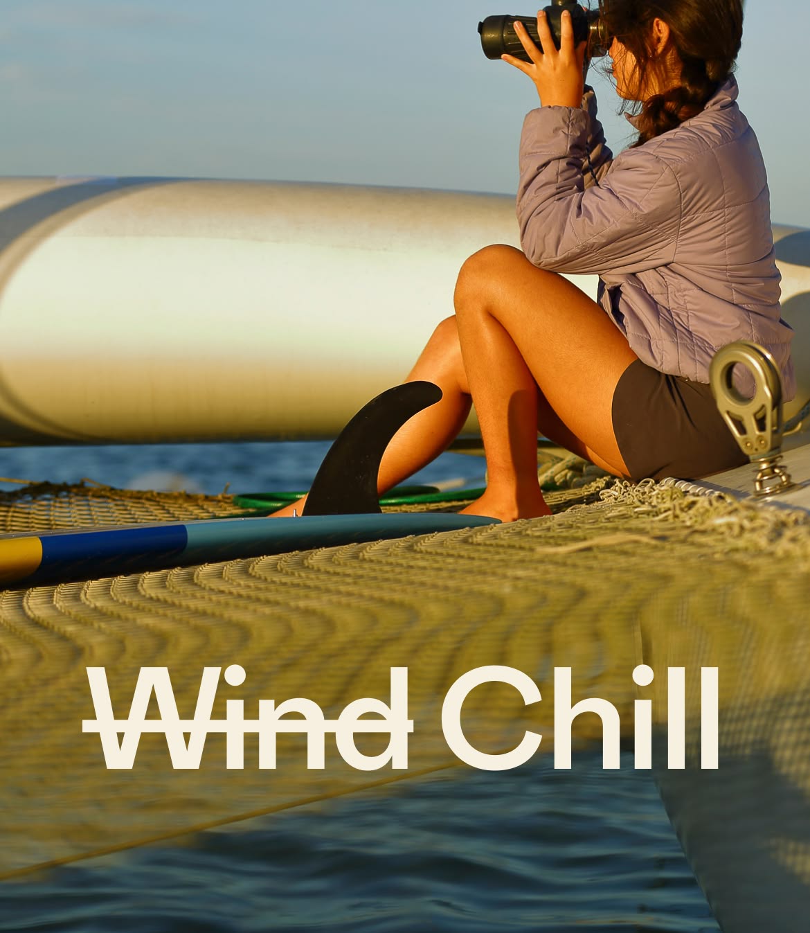A person sits alongside a single-fin surfboard on a boat looking out at the water through binoculars.