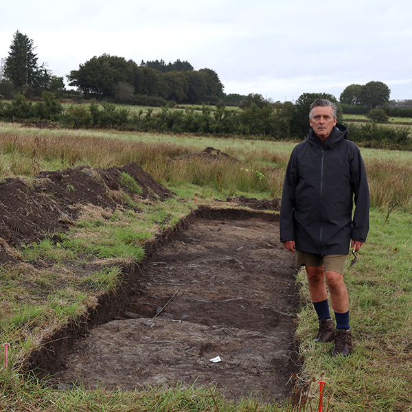 Man stands next to Roman fort remains in field.