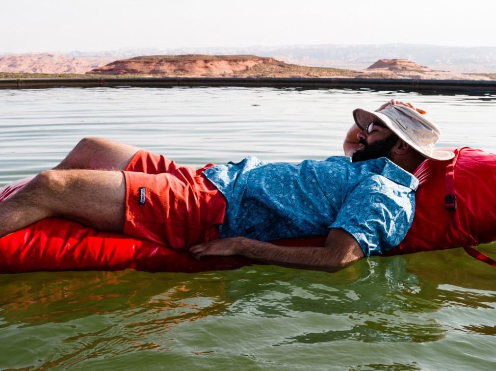 A person floats on a small air mattress in a lake in the desert.