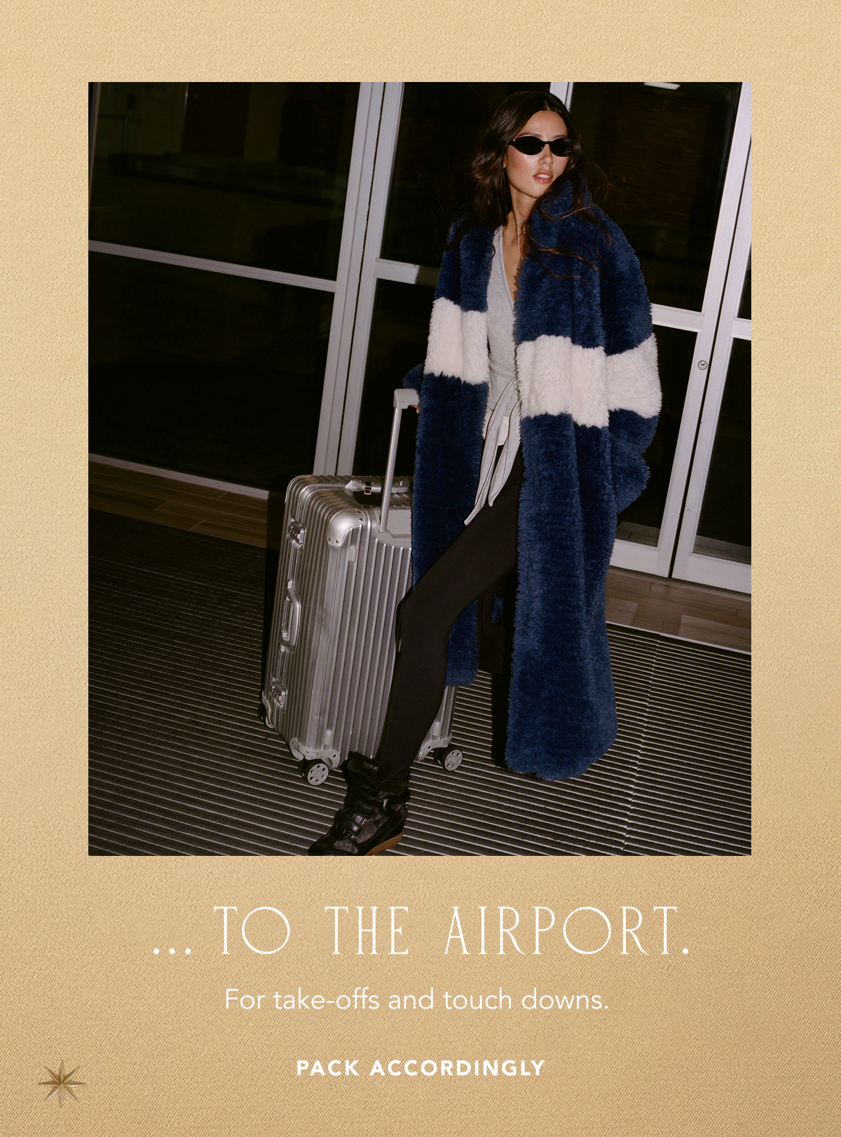 Model at an airport wearing a long navy and white striped plush faux-fur coat, black sunglasses, grey top, leggings, and black boots while posing with a silver aluminum rolling suitcase, with text below reading "... TO THE AIRPORT. For take-offs and touch downs. PACK ACCORDINGLY".