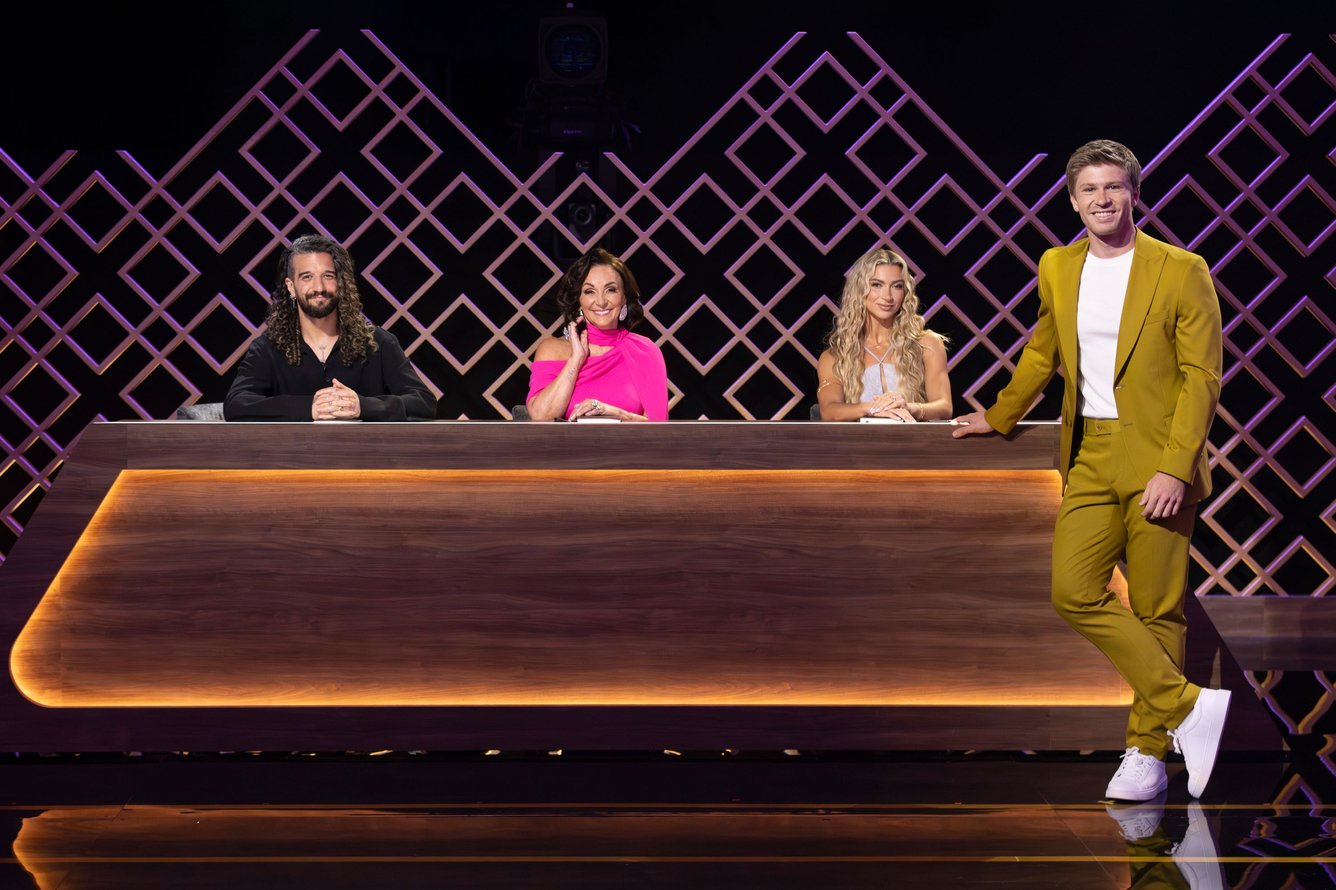 Mark Ballas, Shirley Ballas, and Daniella Karagach sit behind a judges' desk, while host Robert Irwin stands in front of the desk in a chartreuse suit. 