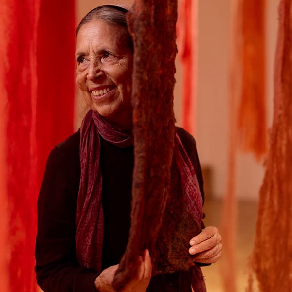 Woman smiling among hanging red and orange textile strands in an art installation.