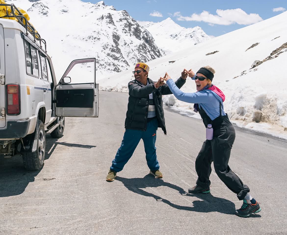 Two people laugh while giving a high five on a mountain pass.