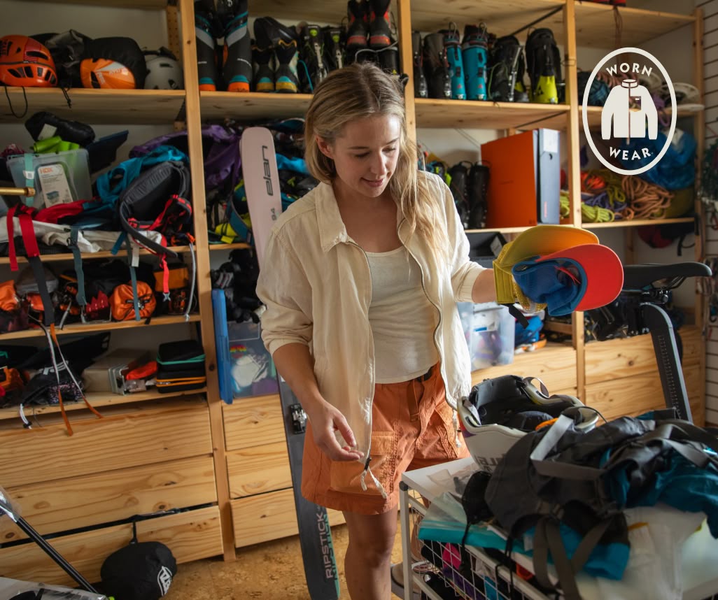 Worn Wear. A person sorts gear in a gear room full of ski boots, rope and other outdoor equipment.