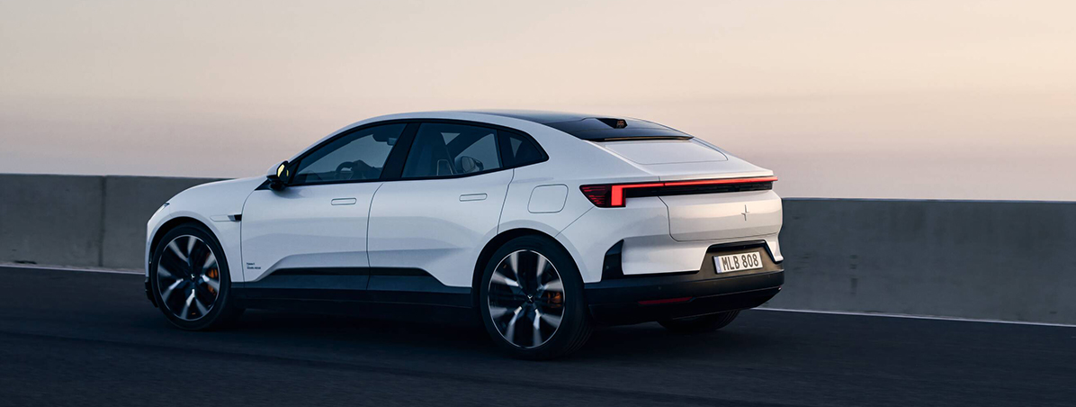 Polestar 4 driving on a road with a concrete barrier at sunset.
