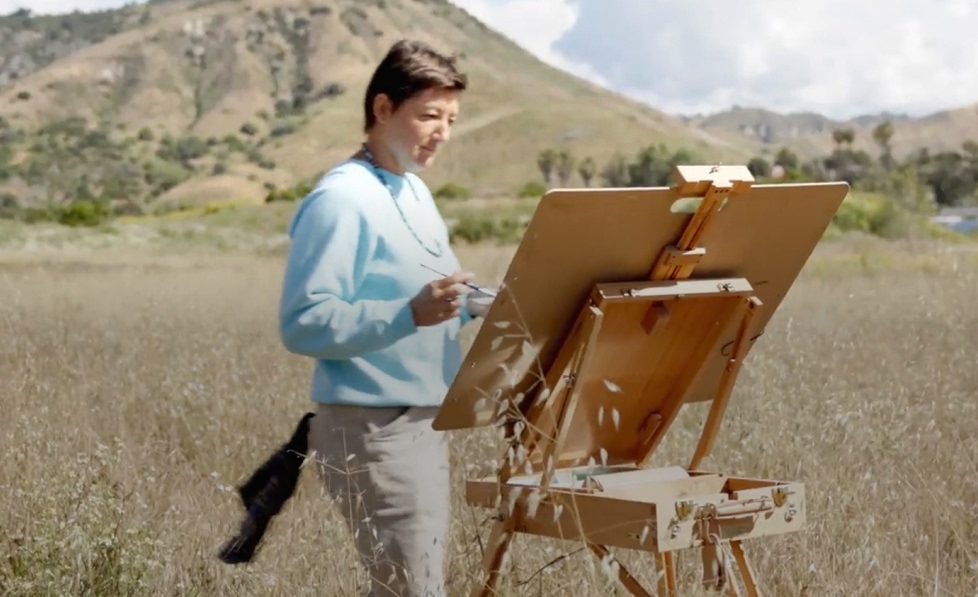 An artist painting in a grassy field.
