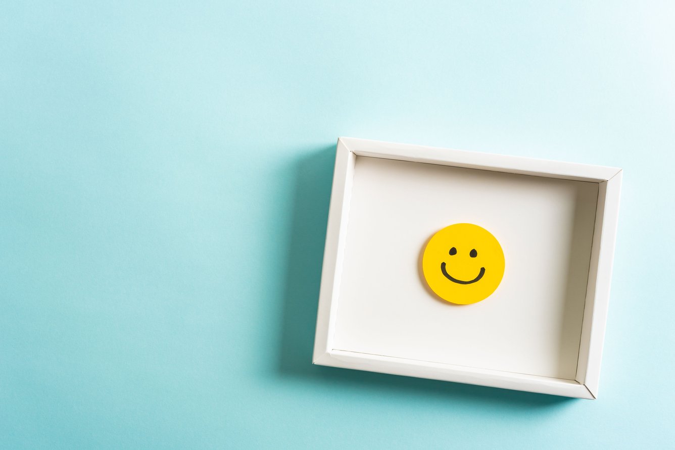 A cut-out yellow smiley face in a box against a blue background