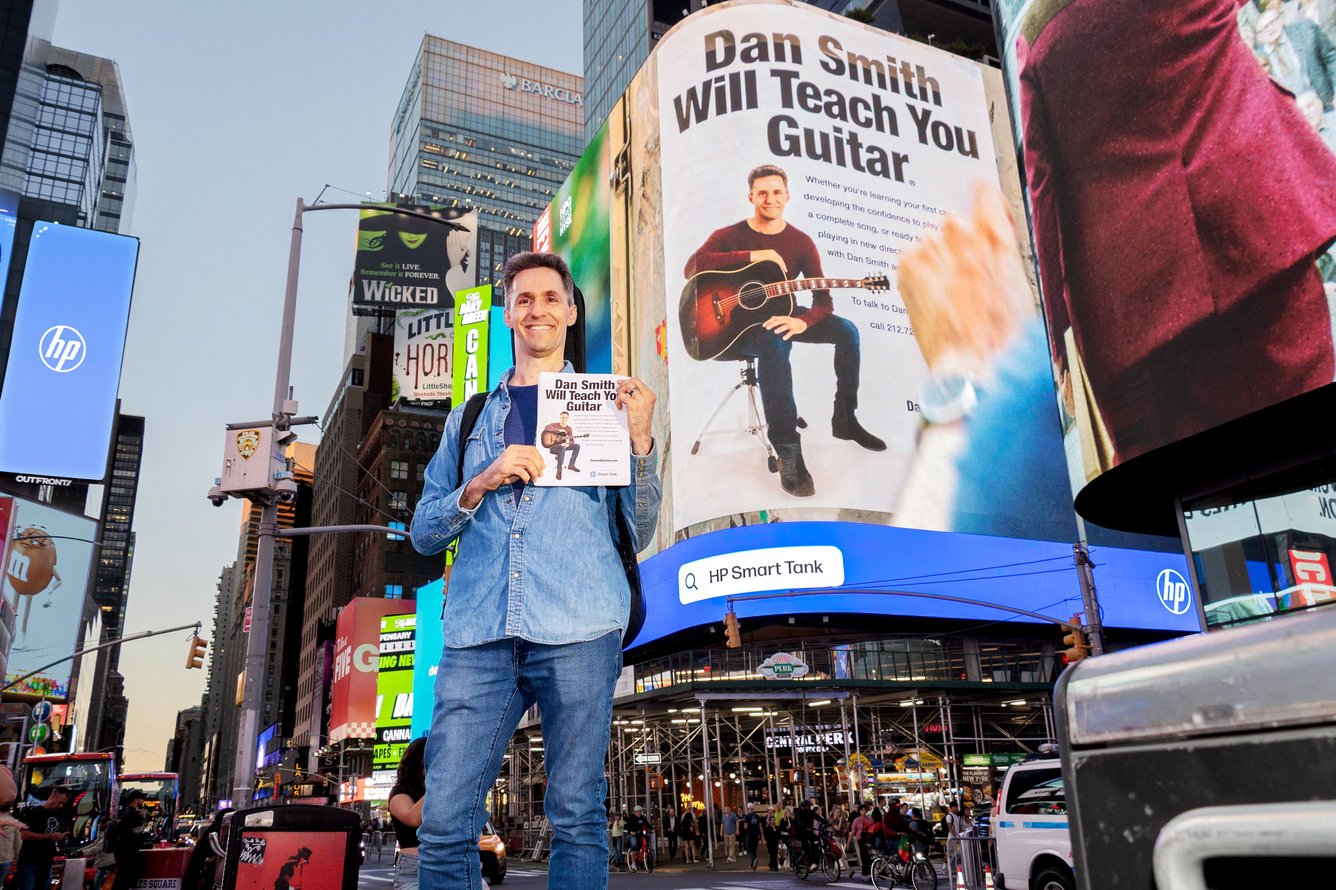 Dan Smith holds up a flyer in front of a Times Square billboard that displays the same flyer.