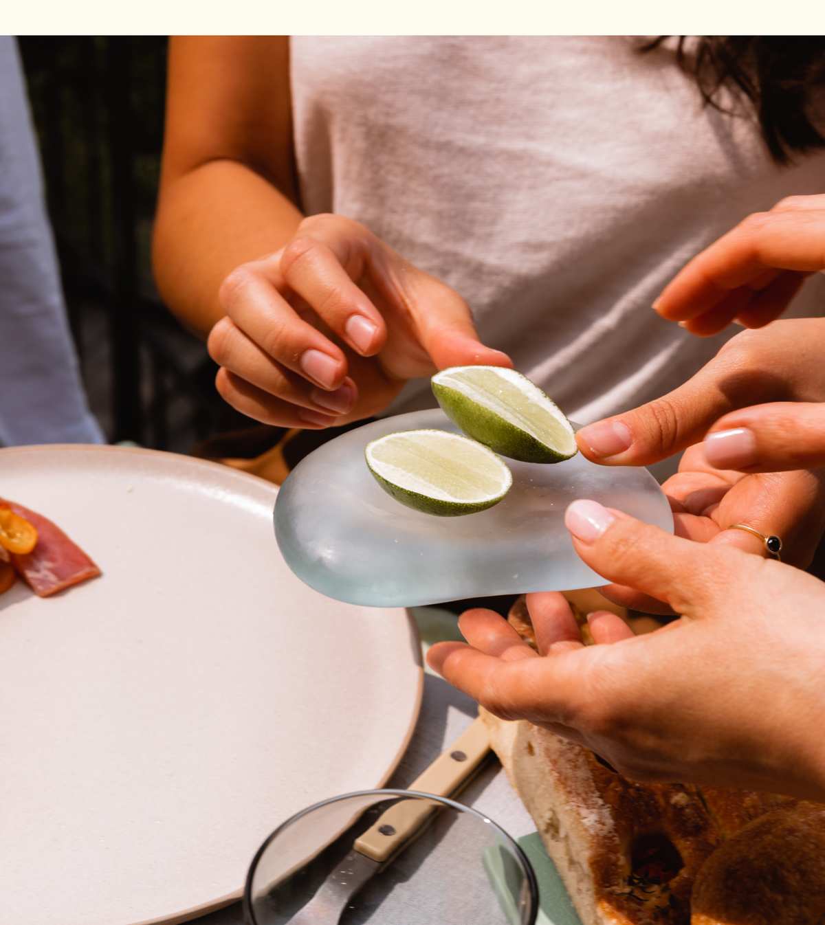 Hands passing a frosted sea glass Resting Stone holding lime wedges at a dinner table, beside bread and a plate.