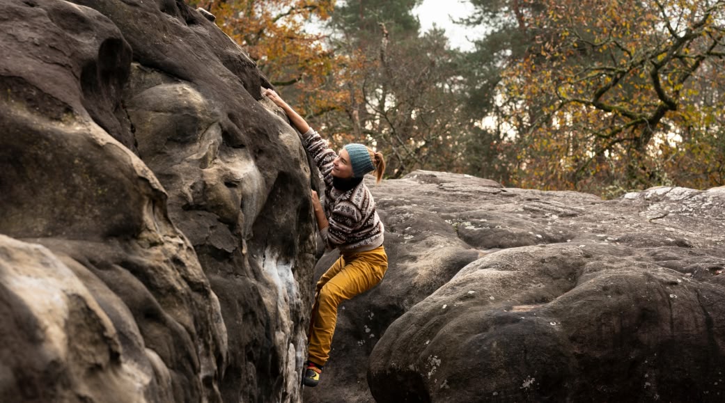 A person climbs a boulder on a cool autumn day.
