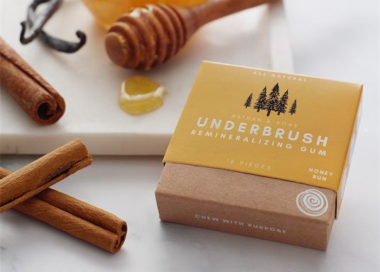 A Honey Bun gum box next to a honey dipper and cinnamon sticks