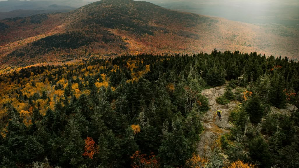 A mountain biker descends a rock face in a mountainous forest in fall colors.