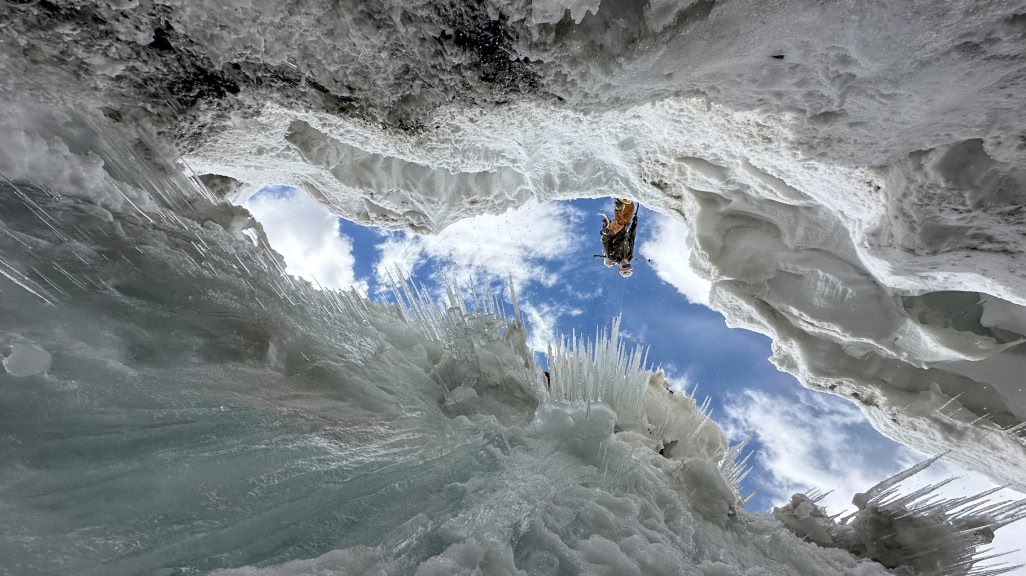 A mountaineer stands on the edge of a bergschrund and looks down toward the camera.