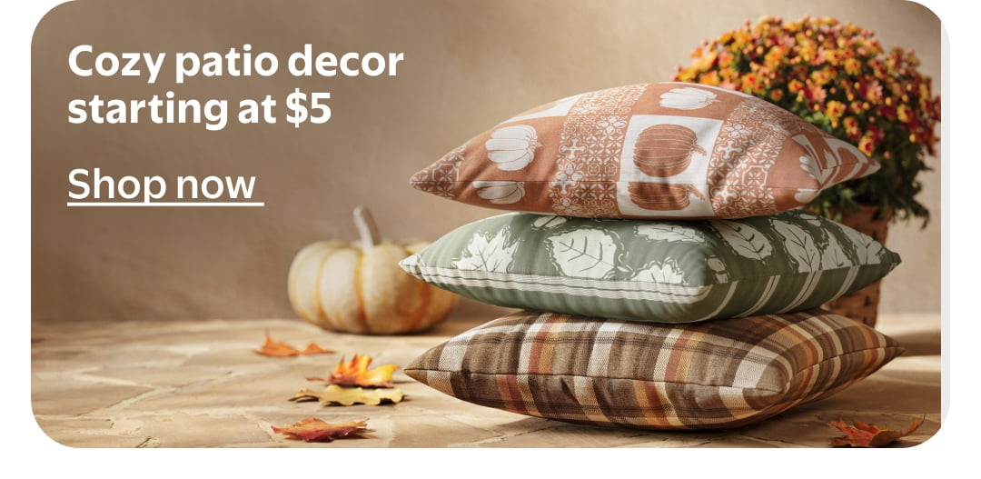 Cozy patio decor starting at $5. Three fall leaf and plaid pillows stacked on a patio with a pumpkin and orange flowers.