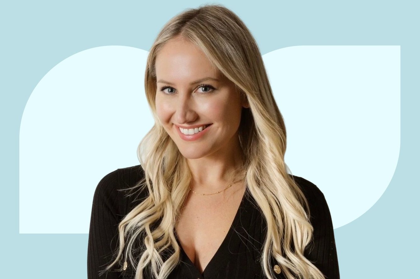 Headshot of Justine Frostad, a light-skinned woman with long wavy platinum blonde hair parted in the middle, wearing a black top smiling at the camera.