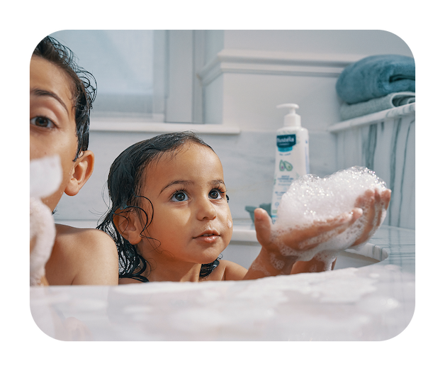 A brother and sister blowing bubbles with a Mustela product in the background