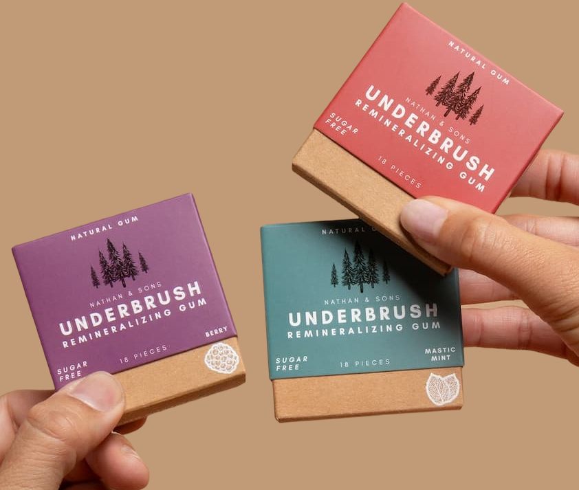 Hands holding three Underbrush gum boxes