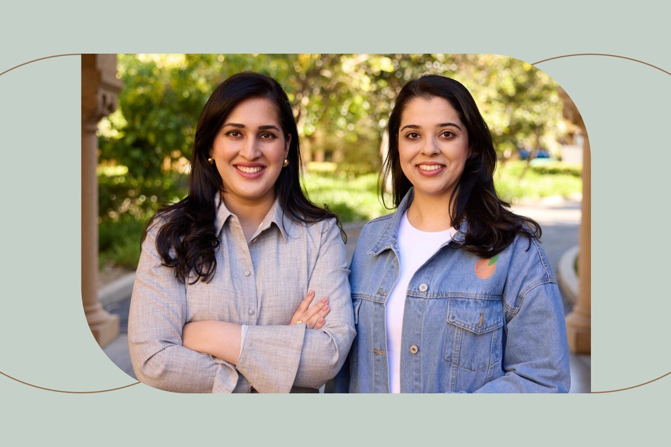 Headshot of sisters Misbah and Farah Uraizee, women with light-medium skin and dark brown straight hair standing side by side while smiling widely at the camera.
