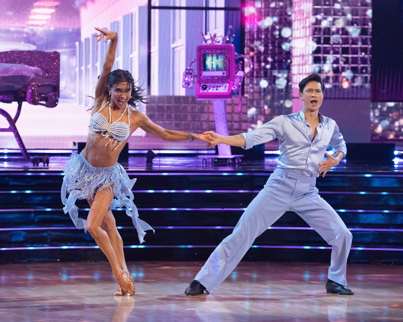 Dancer Jenna Johnson hits a move while holding hands with partner and celebrity Harry Shum Jr., both dresses in coordinating blue outfits. 