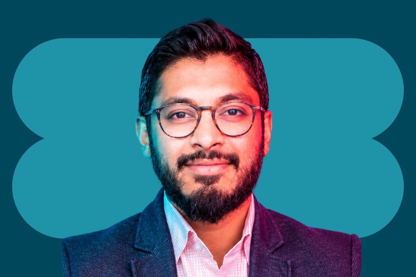 Headshot of Raqib Sheikh, a medium-skinned man with slicked back dark brown hair, short beard and mustache, wearing round glasses and a button-down shirt and blazer.