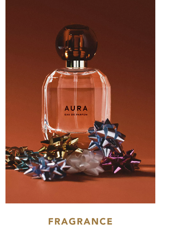 Clear glass bottle of "AURA" Eau de Parfum with a round dark brown cap surrounded by metallic foil gift bows in various colors on a rust-brown background, with text below reading "FRAGRANCE".